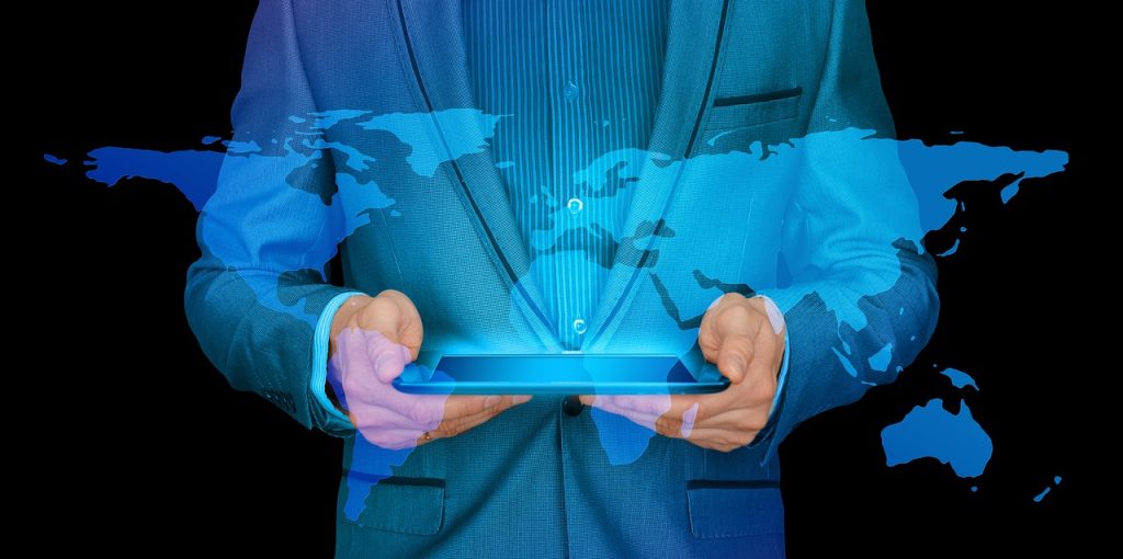 Individual in a suit holding a tablet. World map is overlayed over the person.